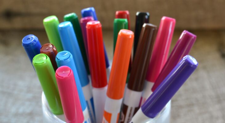 Colorful white board dry erase magic markers in a container on a desk.