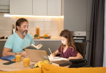 Girl in wheelchair is writing dictation near an adult man