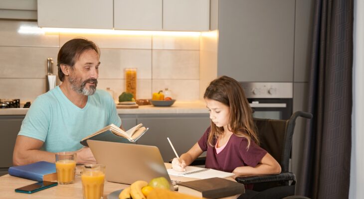 Girl in wheelchair is writing dictation near an adult man