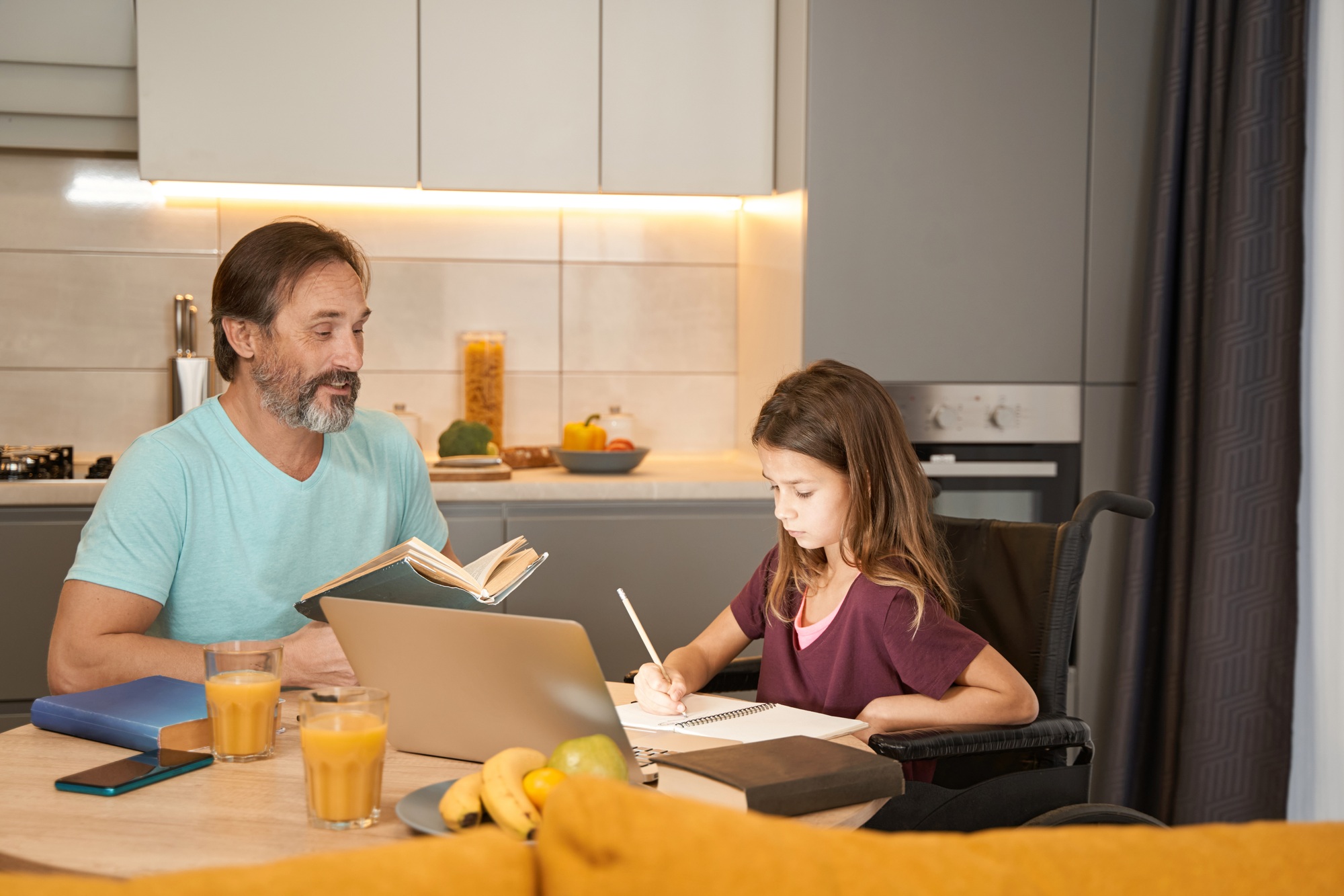 Girl in wheelchair is writing dictation near an adult man