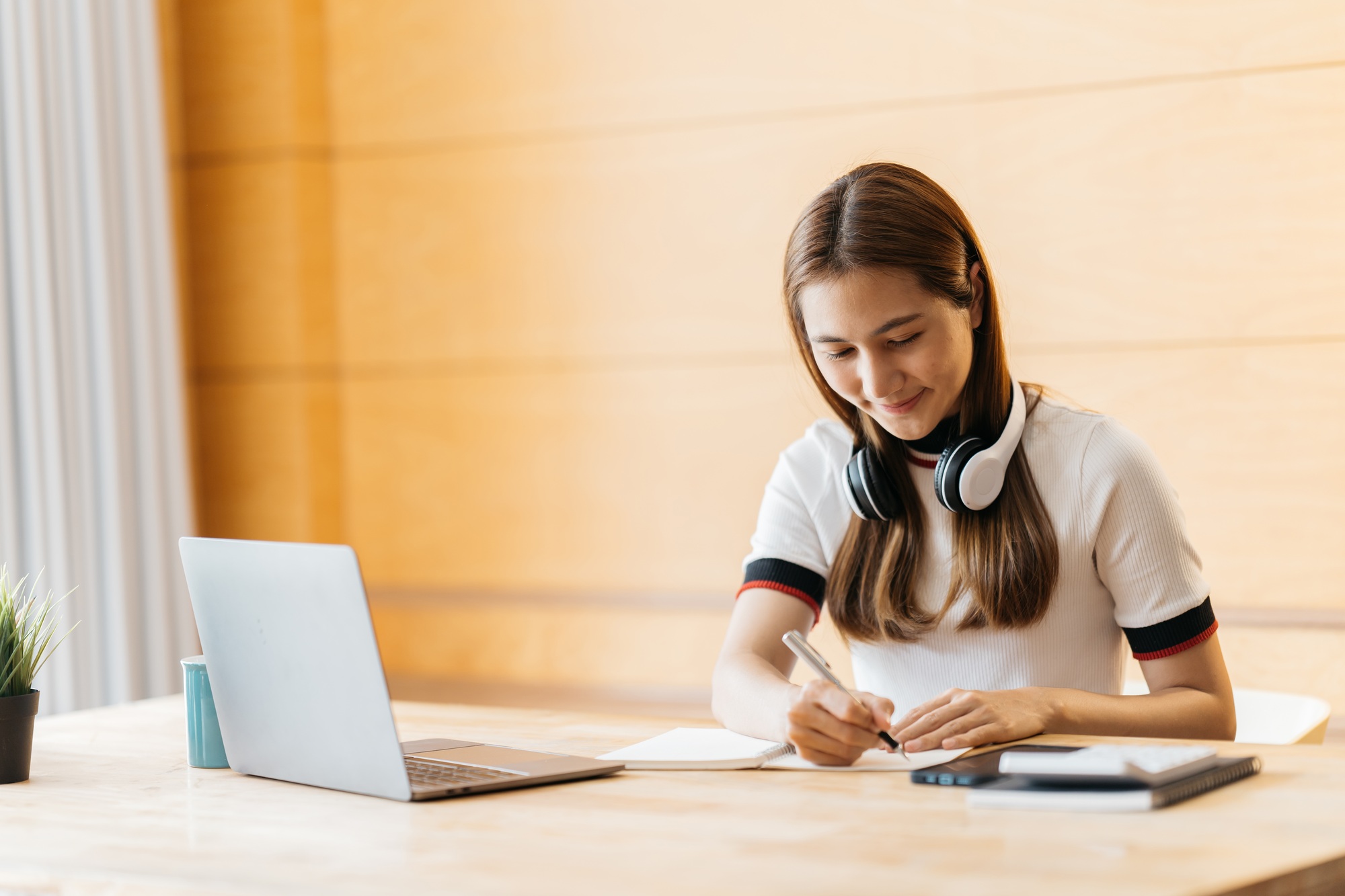 Happy asian businesswoman wearing headset make notes talk by conference call doing video chat on lap