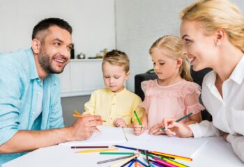happy parents with two little kids drawing with colored pencils at home