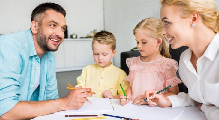 happy parents with two little kids drawing with colored pencils at home