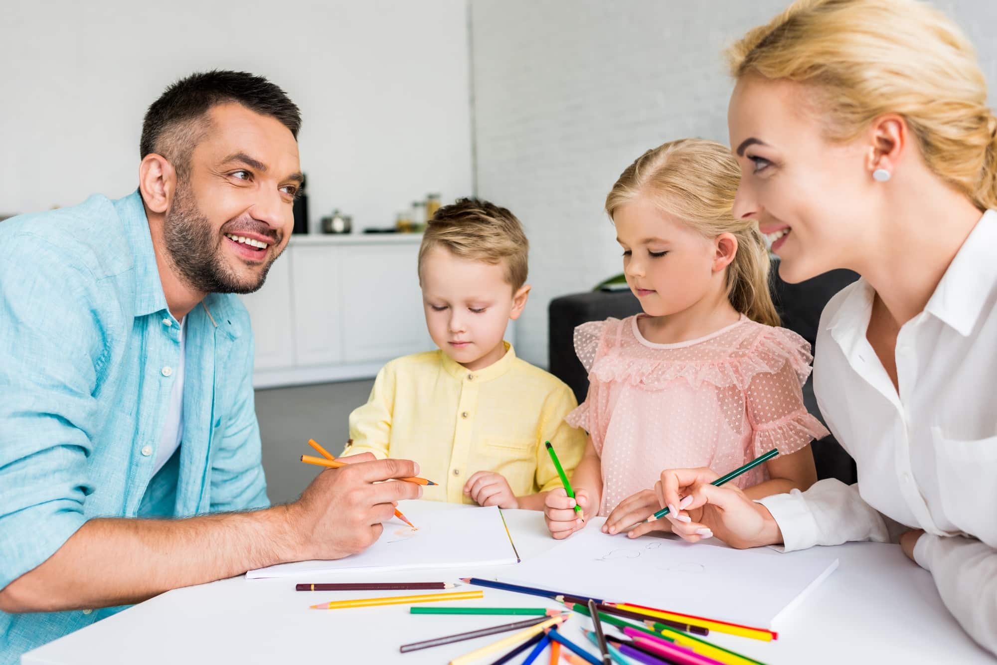 happy parents with two little kids drawing with colored pencils at home