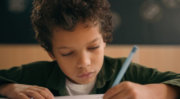 Little African American guy boy writing notes task class lesson primary school write in copybook kid