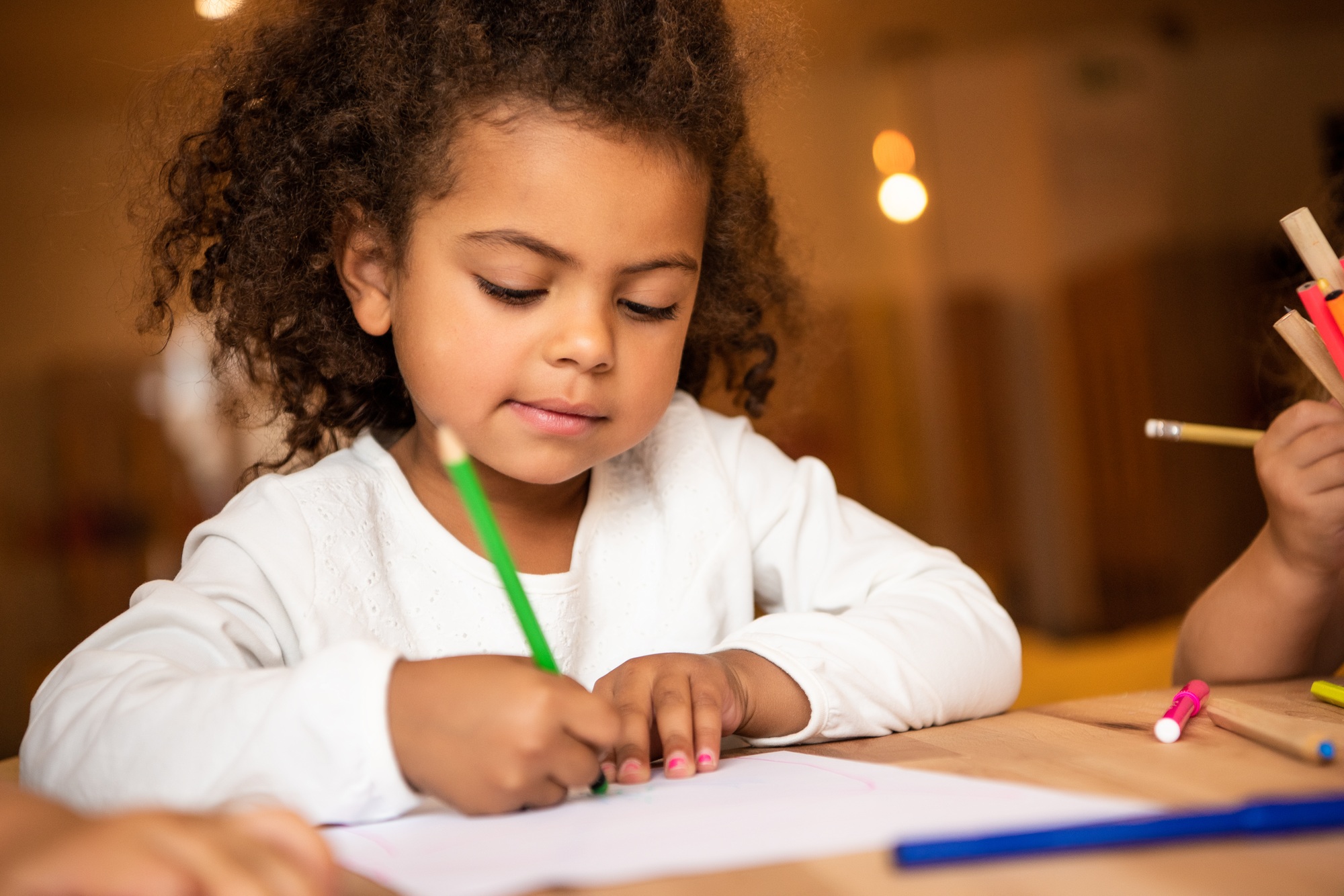 adorable african american kid erasing pencil from sheet of paper in kindergarten