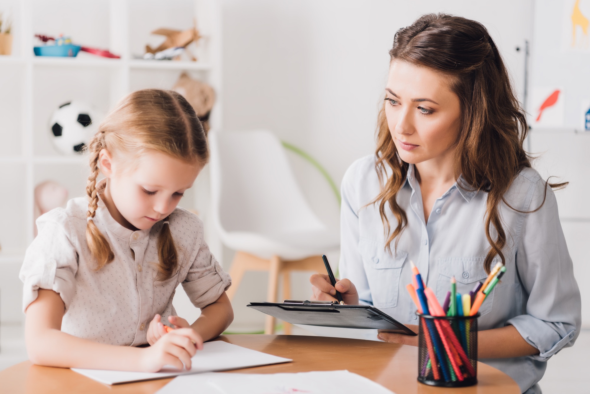 adult psychologist sitting near child drawing with color pencils
