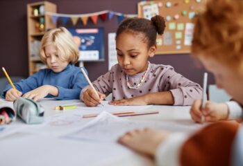Cute African American schoolgirl drawing among her classmates