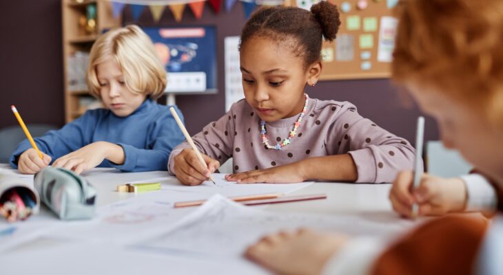 Cute African American schoolgirl drawing among her classmates