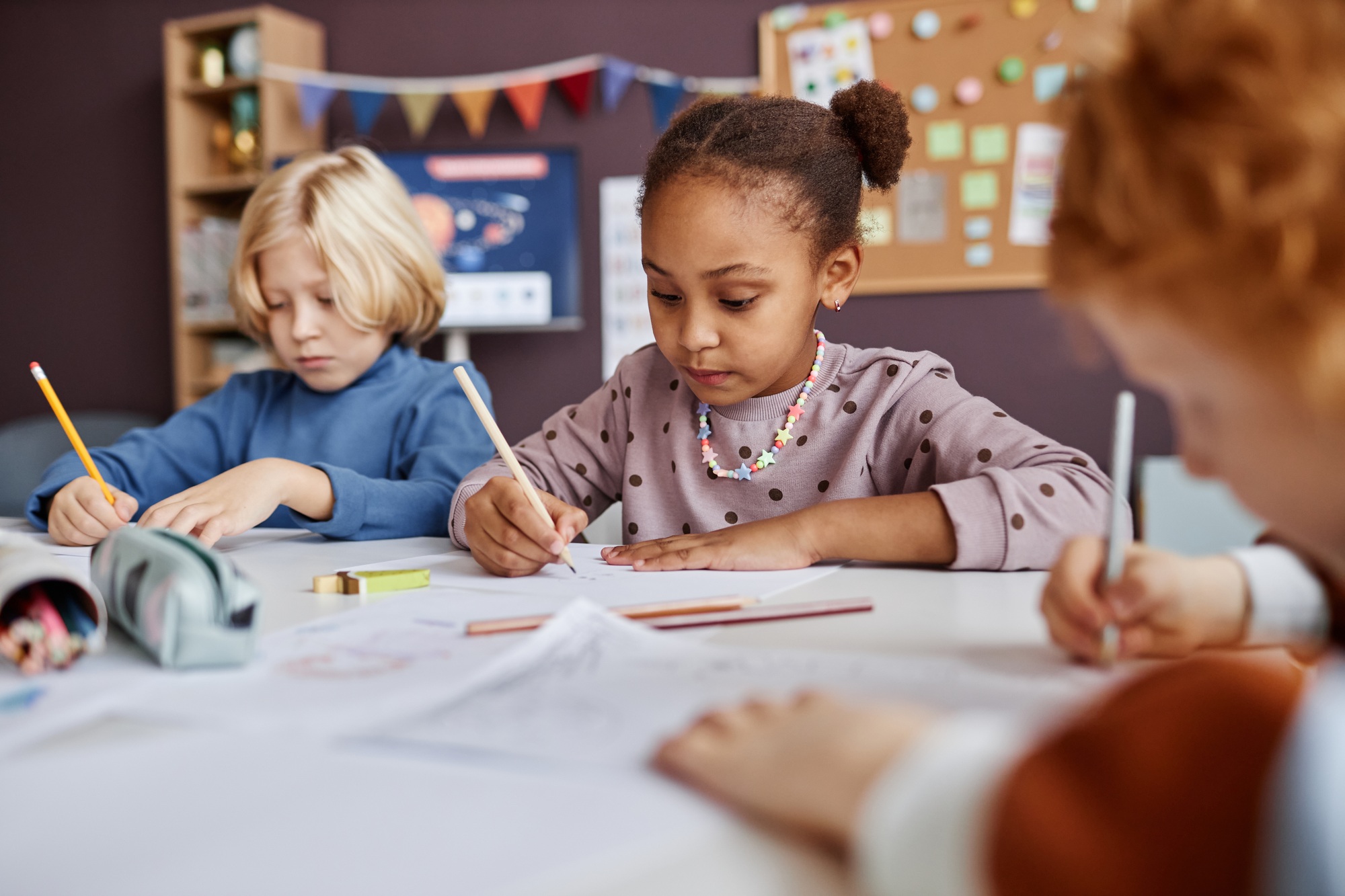 Cute African American schoolgirl drawing among her classmates