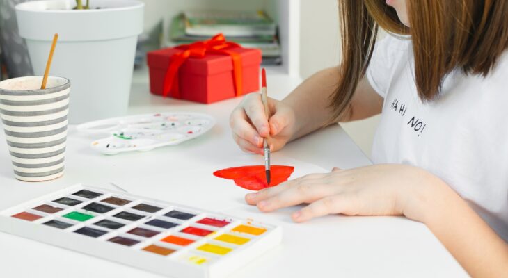 Girl drawing red heart on with watercolors