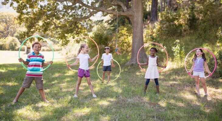 Group of cheerful friends playing with hula hoops at campsite