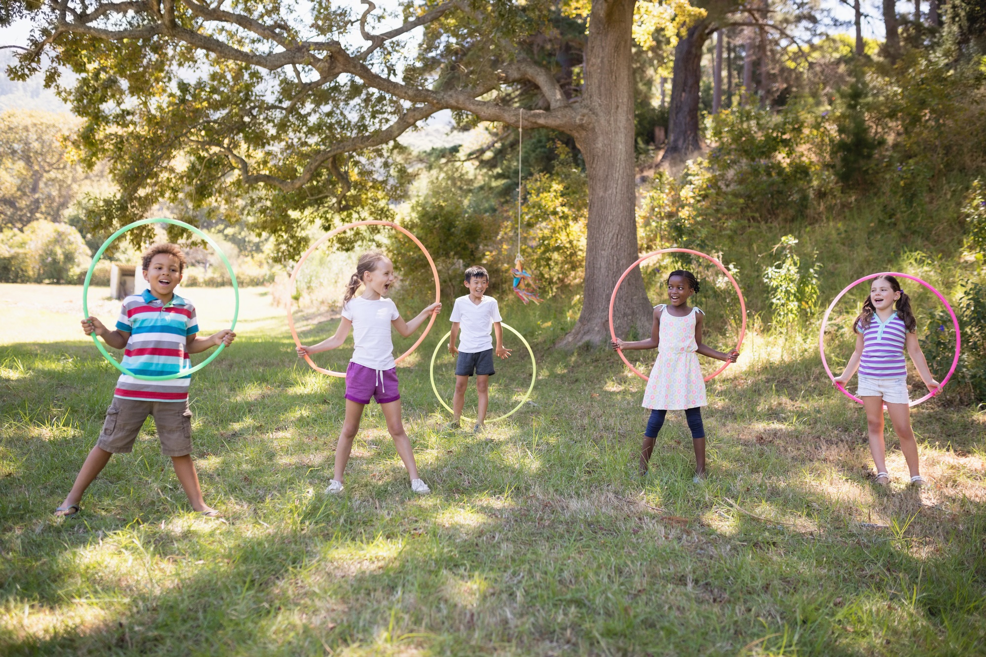 Group of cheerful friends playing with hula hoops at campsite