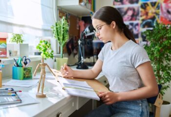 Teenage girl drawing sketches with pencil, sitting at table at home