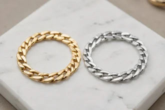 Gourmette enfant en or jaune et en argent sterling posées côte à côte sur un marbre blanc, comparaison des métaux précieux